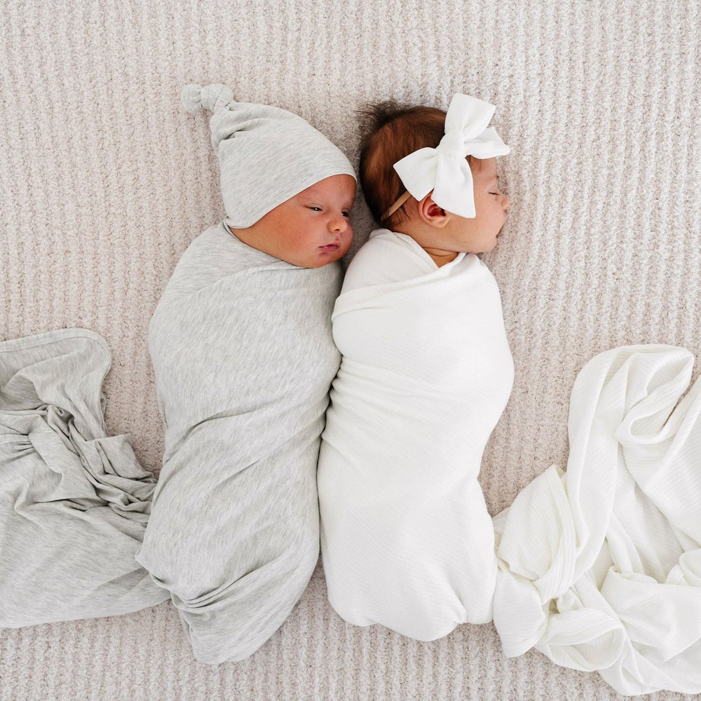 Swaddle blankets. Baby girl in wren ribbed white swaddle blanket. Baby boy in asher swaddle blanket. Laying on blanket