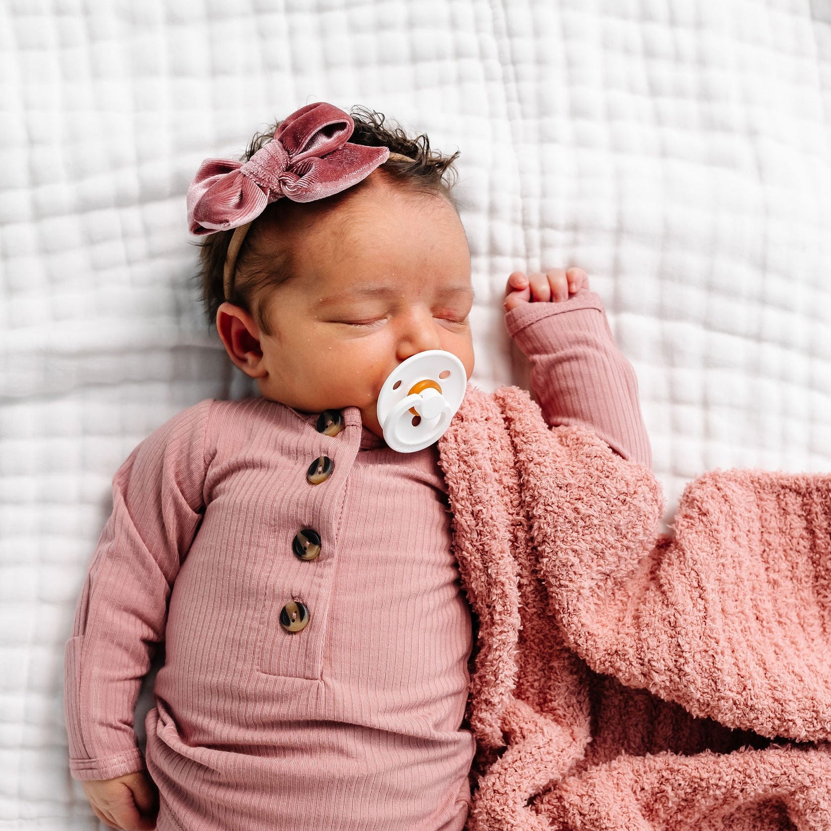 Newborn baby in pink outfit with a pacifier and blanket on a white background