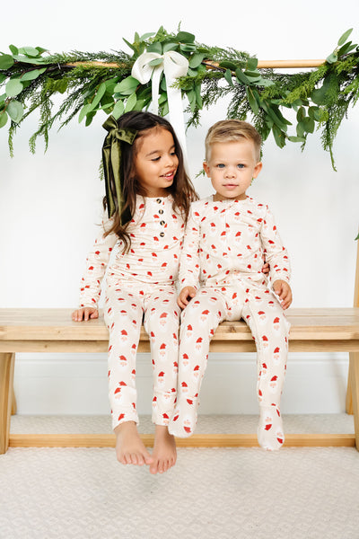 Two children in matching pajamas sitting on a wooden bench with greenery above.