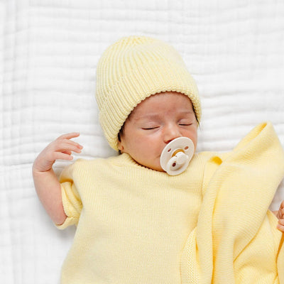 Newborn baby in yellow outfit and hat lying on a white blanket