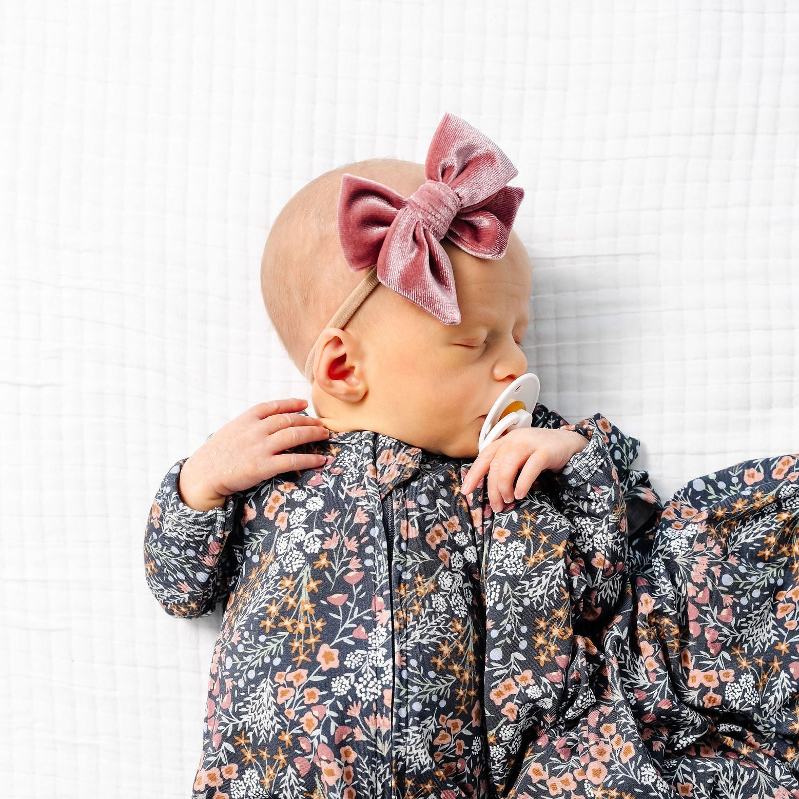 Baby in a floral outfit lying on a white textured surface