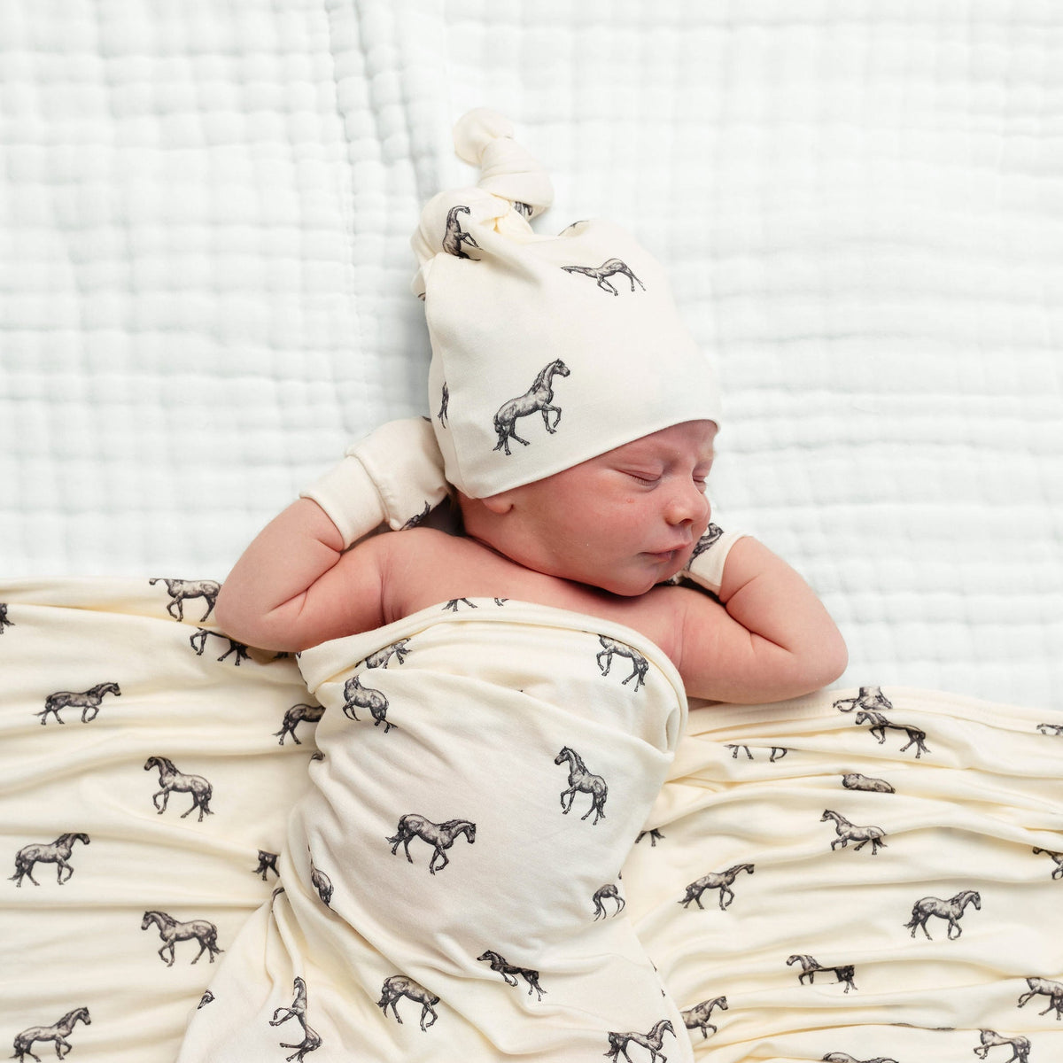 Newborn baby swaddled in a blanket with horse pattern, wearing a matching hat.
