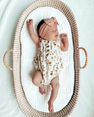 Baby Girl in Rachel Cloud Muslin Bubble Romper with an audrey headband laying in a bassinet